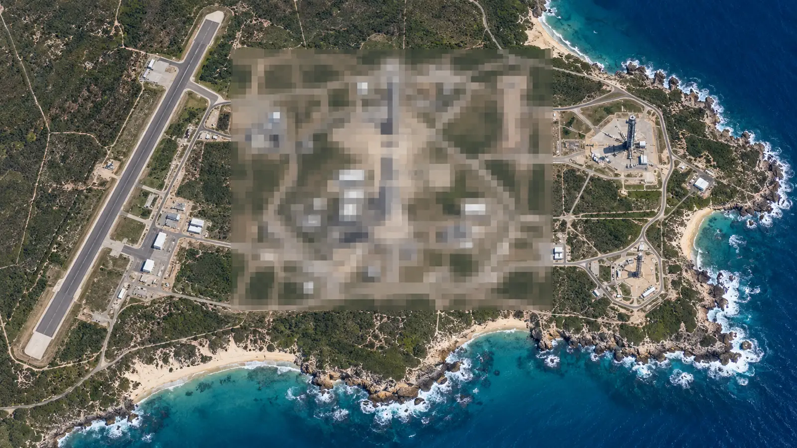 Satellite view of a coastal rocket launch site with its central area pixelated, illustrating Apple Maps blurring military bases